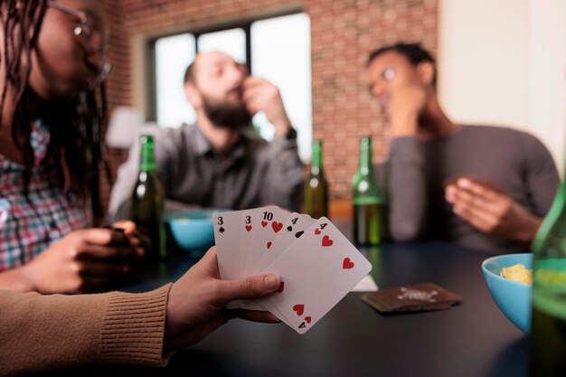 Primer plano de la mano de una mujer sosteniendo juegos de cartas mientras disfruta de una divertida actividad de ocio con los mejores amigos. Persona jugando juegos de cartas con personas que toman bocadillos y bebidas mientras están sentados en casa.