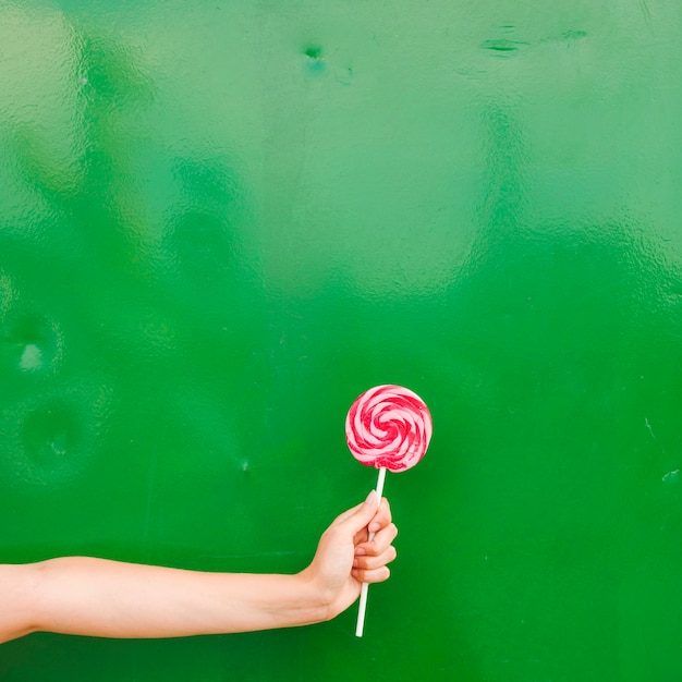 Primer plano de la mano de la mujer sosteniendo la paleta en mano contra el fondo verde