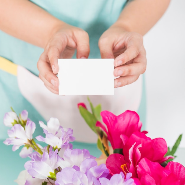 Primer plano de la mano de una mujer sosteniendo una tarjeta de visita en blanco sobre flores de colores