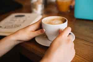 Foto gratuita primer plano de la mano de la mujer sosteniendo la taza de café en la mesa