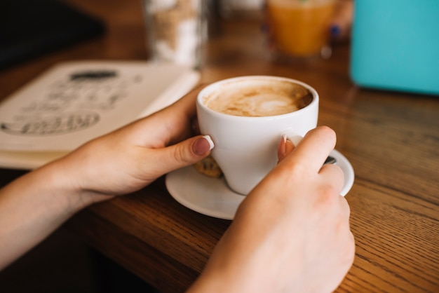 Primer plano de la mano de la mujer sosteniendo la taza de café en la mesa