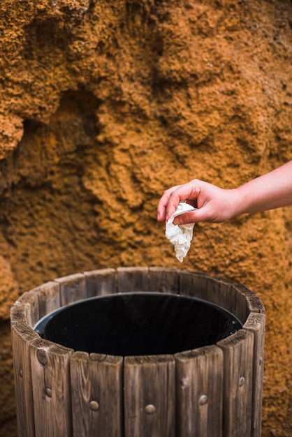 Primer plano de la mano de la mujer tirando papel blanco en la basura de madera