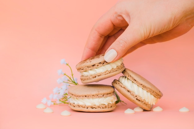 Primer plano de la mano de la mujer tomando los macarrones contra el telón de fondo de coral