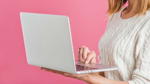 Primer plano de la mano de una mujer usando una computadora portátil sobre fondo rosa