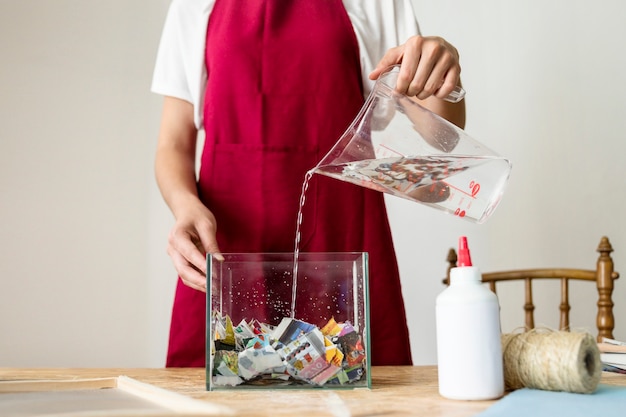 Primer plano de una mano de mujer vertiendo agua en trozos de papel en el taller