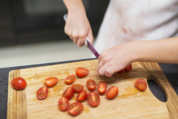 Primer plano de la mano de una niña cortando tomates con un cuchillo en una tabla de cortar