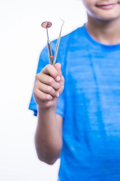 Primer plano de la mano de un niño con raspador y espejo dental