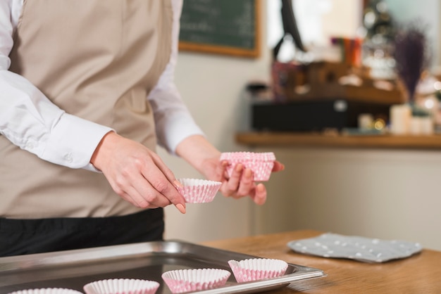 Primer plano de una mano de panadero femenina colocando cajas de cupcakes en la bandeja para hornear en mesa de madera