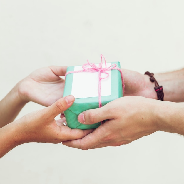 Foto gratuita primer plano de la mano de la pareja con caja de regalo verde sobre fondo liso