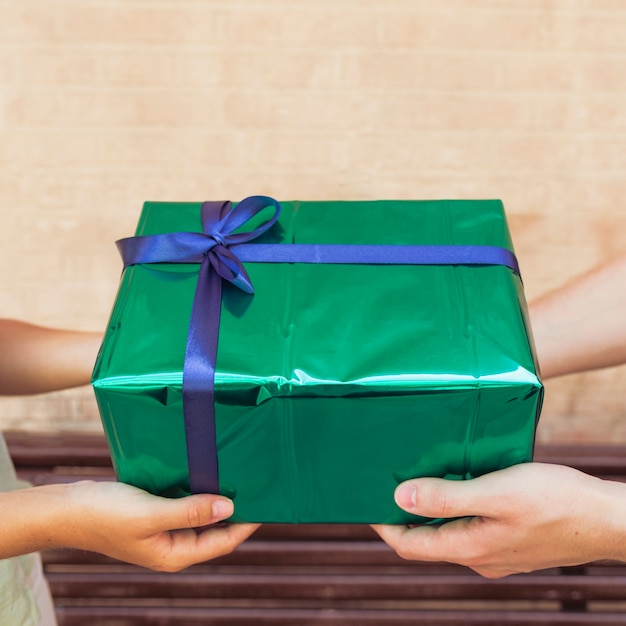 Primer plano de la mano de una pareja con caja de regalo verde