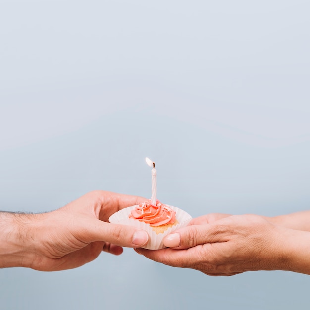 Primer plano de la mano de la pareja con muffins con una vela iluminada sobre fondo gris