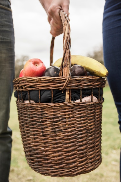 Primer plano de la mano de la pareja sosteniendo la cesta de picnic llena de frutas