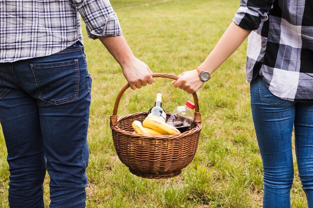 Primer plano de la mano de la pareja sosteniendo la cesta de picnic en el parque