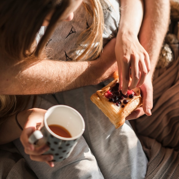 Primer plano de la mano de la pareja sosteniendo pasteles al horno y una taza de café