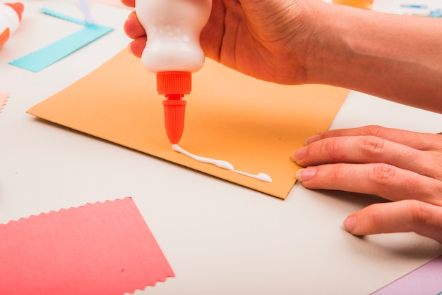 Primer plano de la mano de una persona aplicando pegamento blanco sobre papel