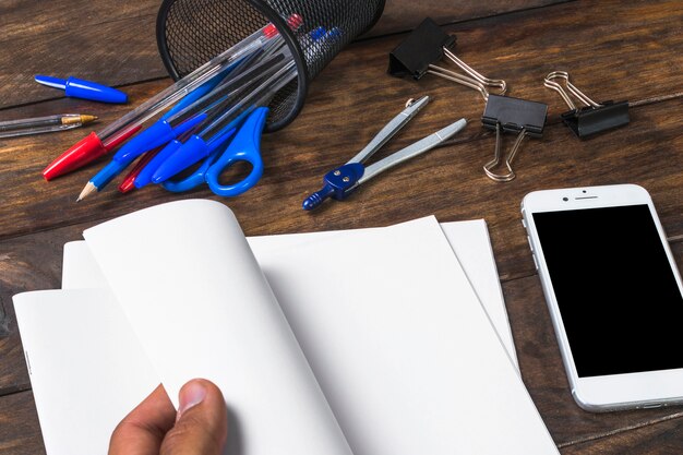 Primer plano de la mano de la persona convirtiendo el libro blanco con papelería y teléfono móvil