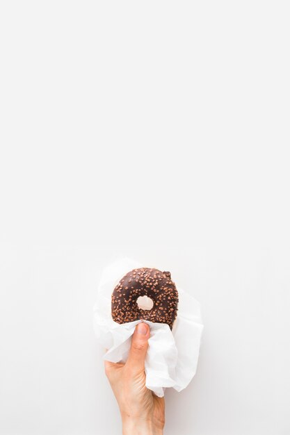 Primer plano de la mano de una persona con donut de chocolate en papel de seda sobre fondo blanco