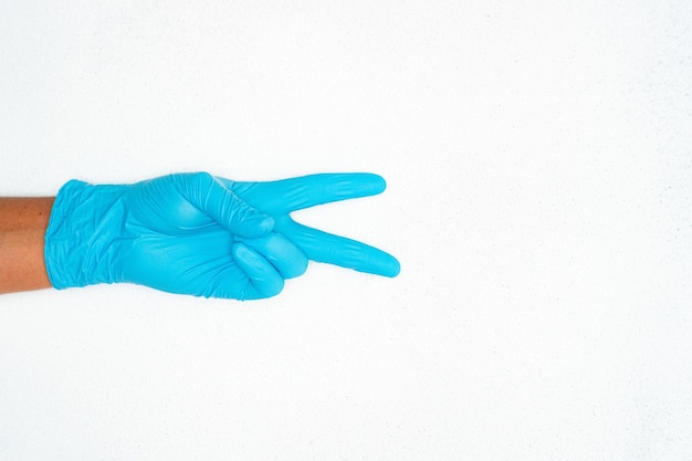 Primer plano de la mano de una persona con guantes médicos azules que muestran un signo con las manos cerca de un espacio de copia