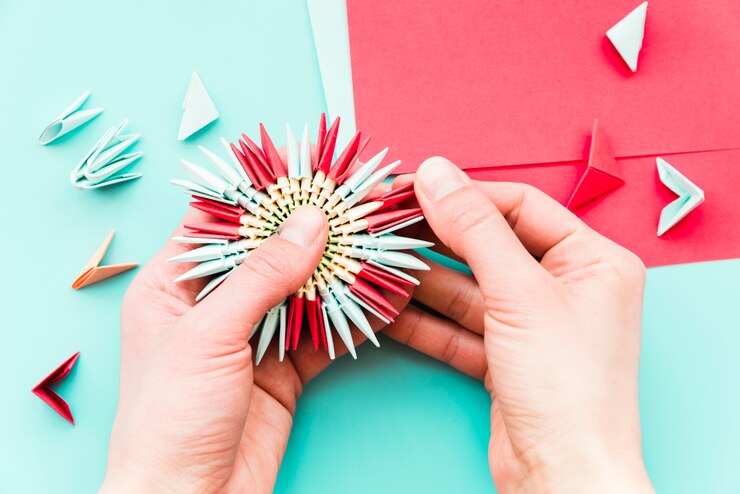 Foto gratuito primer plano de la mano de una persona haciendo la flor de papel sobre fondo verde azulado
