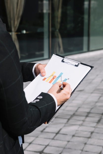 Primer plano de la mano de una persona de negocios que dibuja una flecha creciente en un gráfico sobre el portapapeles