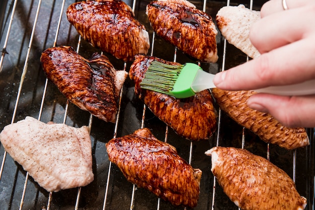 Primer plano de la mano de una persona que aplica aceite a las alitas de pollo asadas con cepillo