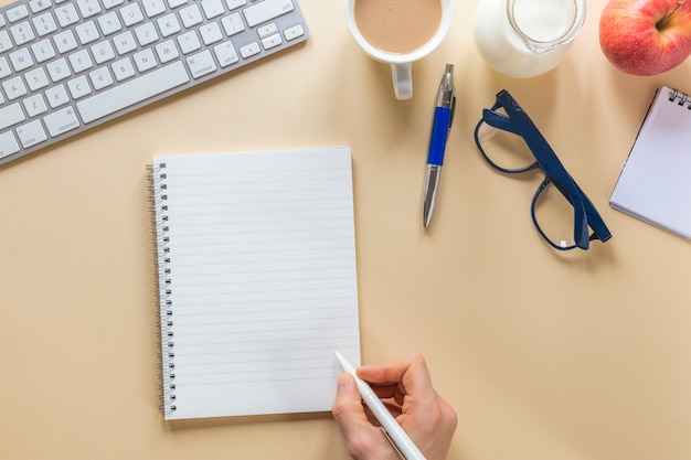 Primer plano de la mano de una persona que escribe en una libreta espiral con una pluma en el escritorio de oficina beige