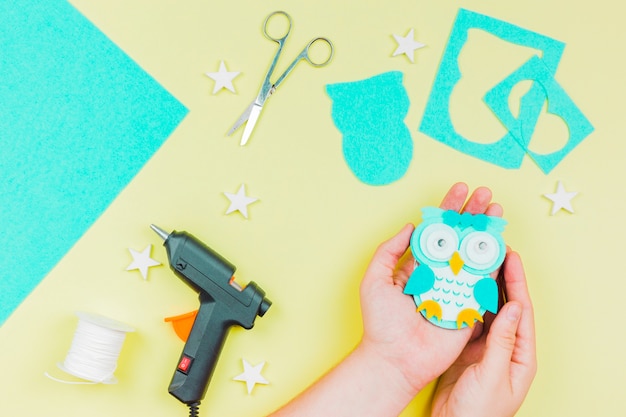 Primer plano de la mano de una persona que muestra un búho lindo de papel azul hecho a mano sobre fondo amarillo