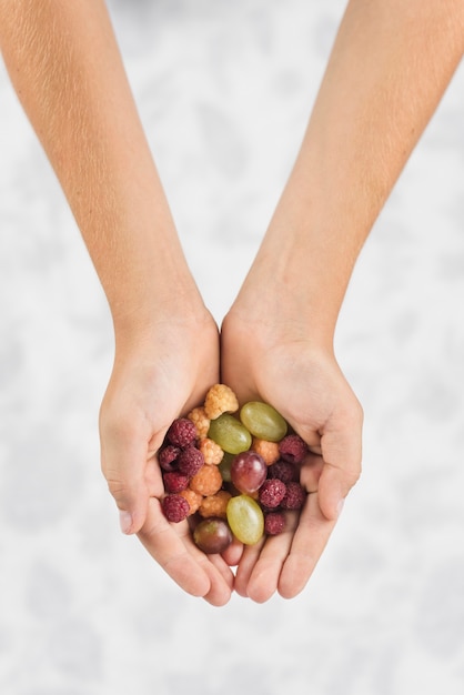 Primer plano de la mano de una persona que muestra frambuesas y uvas