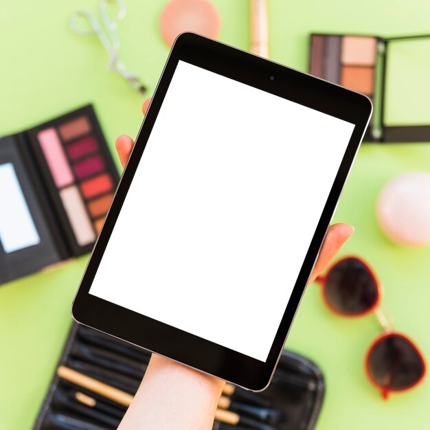 Primer plano de la mano de una persona que muestra la pantalla de la tableta digital en blanco sobre los cosméticos