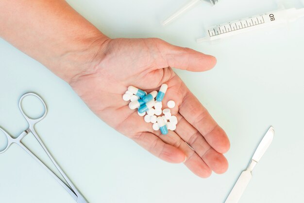 Primer plano de la mano de una persona que muestra píldoras con instrumentos médicos sobre fondo blanco