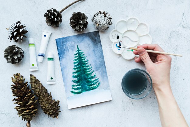 Primer plano de la mano de una persona que pinta árboles de navidad con pintura acrílica