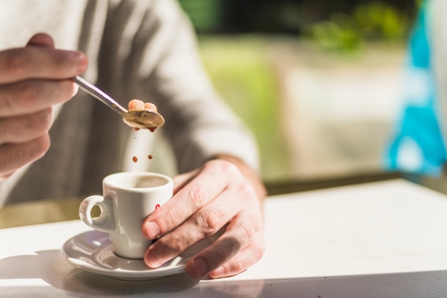 Primer plano de la mano de una persona que pone azúcar moreno en el té de hierbas rojo