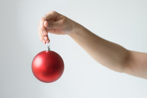 Primer plano de la mano de la persona que sostiene la bola roja de la Navidad