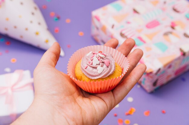 Primer plano de la mano de una persona que sostiene muffins decorativos contra el fondo borroso