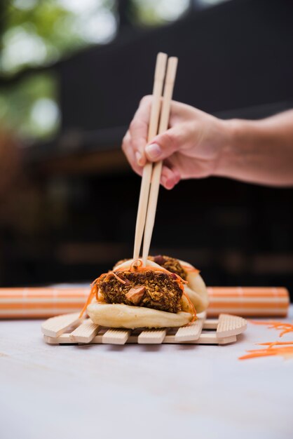 Primer plano de la mano de una persona que sostiene los palillos sobre la bola de masa hervida hervida con relleno de carne y verduras