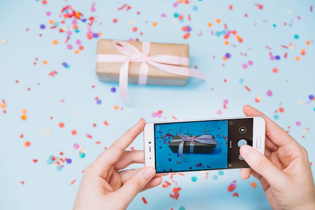 Primer plano de la mano de una persona que toma una foto de una caja de regalo en un teléfono inteligente