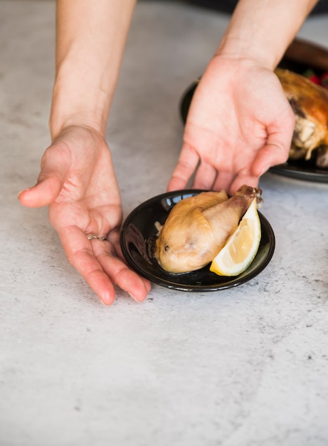 Primer plano de la mano de una persona que toma un plato de pollo asado con una rodaja de limón