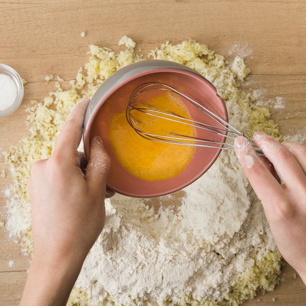 Primer plano de la mano de una persona que vierte los huevos batidos en queso rallado y harina para preparar ñoquis italianos