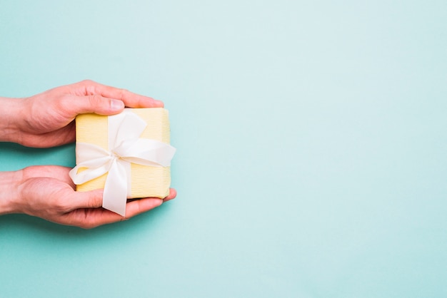 Primer plano de la mano de una persona sosteniendo una pequeña caja de regalo sobre fondo azul