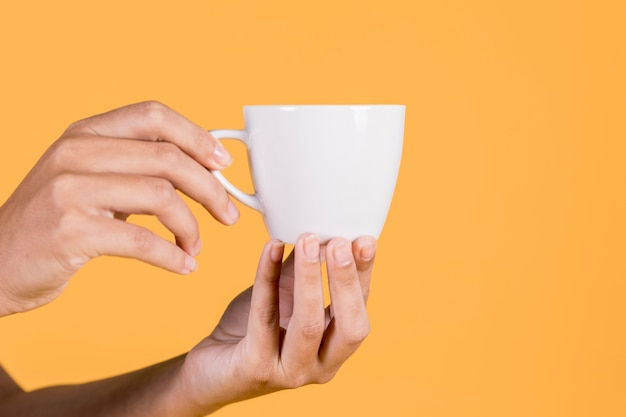 Primer plano de la mano de la persona sosteniendo la taza de té contra el telón de fondo amarillo