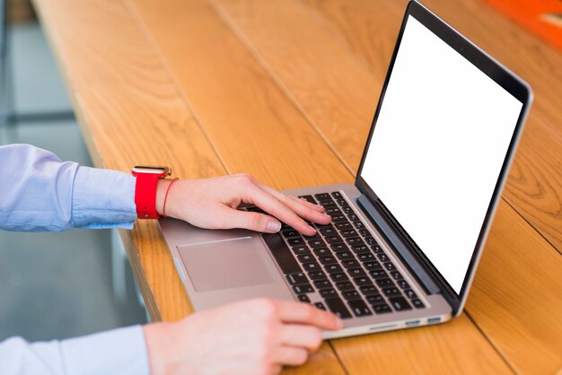 Primer plano de la mano de una persona usando una computadora portátil sobre un escritorio de madera