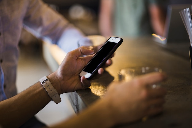 Primer plano de la mano de la persona usando el teléfono celular en el mostrador de la barra