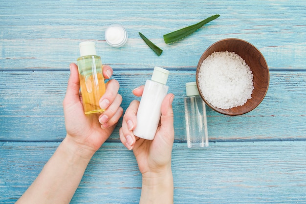 Primer plano de la mano que elige la botella natural del aerosol del balneario en la tabla de madera