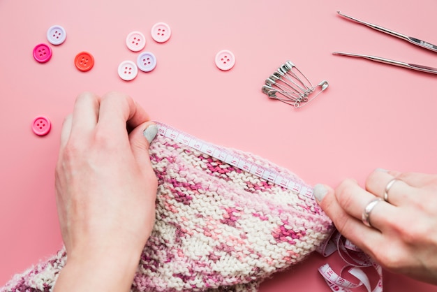 Primer plano de la mano que mide el tejido de punto con cinta sobre fondo rosa