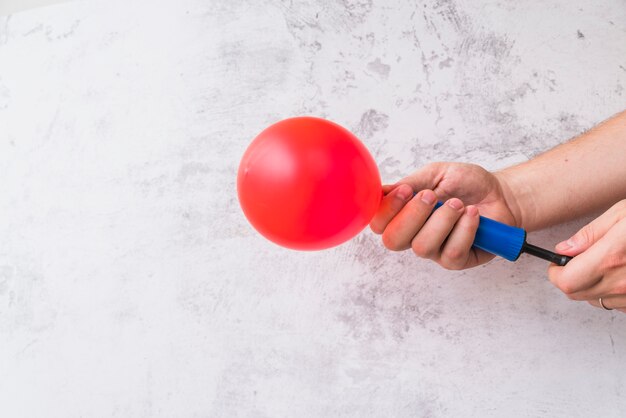 Primer plano de la mano que sopla el globo rojo con la bomba contra la pared