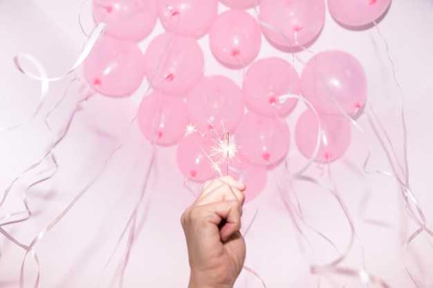 Primer plano de la mano que sostiene una bengala encendida bajo el techo decorativo con globos rosados