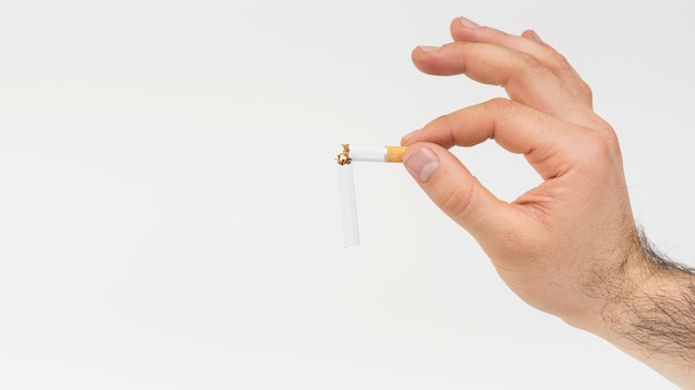 Primer plano de la mano que sostiene el cigarrillo roto contra el fondo blanco