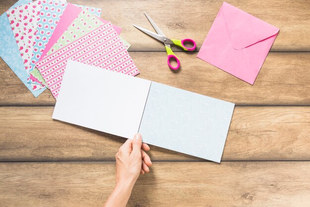 Primer plano de la mano que sostiene el papel de la tarjeta en blanco contra el telón de fondo de madera