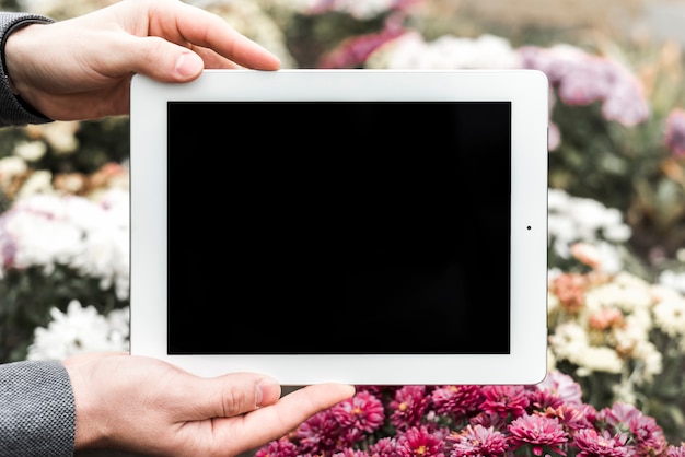 Foto gratuita primer plano de la mano que sostiene la tableta digital frente a las flores