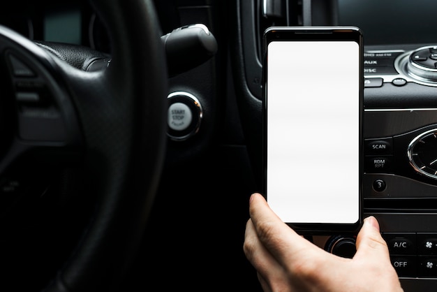 Primer plano de una mano que sostiene el teléfono inteligente que muestra la pantalla en blanco blanca en el coche